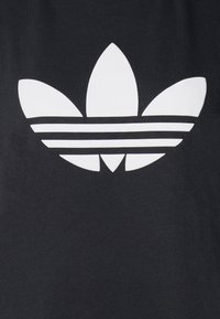 Juodas audinys su dideliu baltu Adidas trefoil logotipu ir trimis horizontaliomis juostelėmis žemiau. Lygus paviršius ir simetriška struktūra.