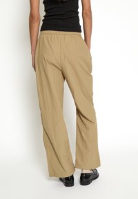 Pantaloni beige a gamba larga realizzati in tessuto leggero, con cinturino elastico in vita e tasche laterali. La texture è liscia e leggermente stropicciata.