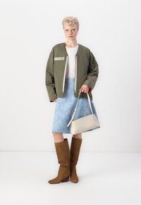 Quilted olive green jacket, white ribbed top, blue floral denim skirt, beige handbag, brown knee-high boots with a chunky heel.