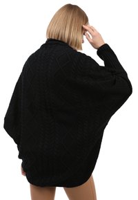 Poncho negro de punto con un patrón de cable texturizado. Presenta mangas anchas y un ajuste holgado, ideal para superponer.