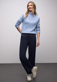Hellblauer Rollkragenpullover mit gerippten Bündchen, kombiniert mit marineblauen, weit geschnittenen Hosen mit Kordelzug in der Taille und Seitentaschen, getragen mit weißen Sneakers.