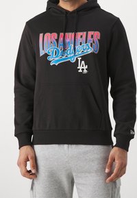 Sweat à capuche noir avec une poche kangourou. Présente des lettres colorées "LOS ANGELES" et "Dodgers". Tissu doux avec des poignets et un ourlet à côtes.