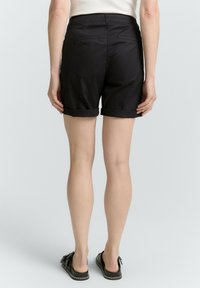 Shorts en coton noir avec des revers roulés, deux poches arrière et une taille ajustée. Texture lisse et style décontracté, adaptés aux temps chauds.