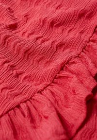 Roter strukturiertes Gewebe mit wavy Mustern und gerafften Rüschendetails schafft eine schichtartige Erscheinung. Weiches, leichtes Material.
