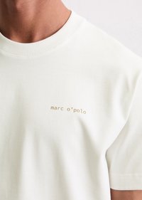 White cotton t-shirt with ribbed crew neckline, featuring gold "marc o'polo" logo on the left chest. Smooth texture, short sleeves.
