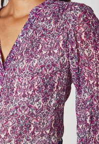Flutter-sleeve blouse in lightweight fabric with intricate purple and pink floral pattern on a light background. V-neckline and pleated detail.