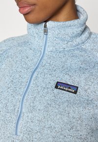 Lichtblauwe ritssluiting fleece met een gemêleerde textuur, hoge kraag en een Patagonia-logo op de borst. Heeft een rechte rits.
