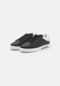 Svarte lærsneakers med hvit gummisåle, med svarte schnørebånd, en hvit detalj på hælen og teksten "EXCHANGE" på siden.