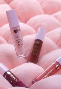 Vier lippenbalsems in verschillende tinten liggen op zacht roze stof: een doorzichtige met een witte dop, een diep bordeauxrood, een zachtroze en een rijke bruine.