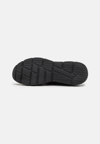 Semelle de chaussure noire avec un motif texturé, présentant des formes hexagonales et rectangulaires, conçue pour l'adhérence et la traction.