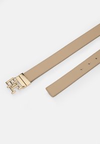 Ceinture en cuir tan avec une boucle en métal doré poli présentant un design géométrique entrelacé et plusieurs trous d'ajustement sur la sangle.