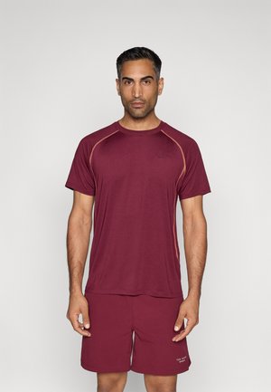 Bordeaux sportt-shirt met korte mouwen en contraststeek. Gecombineerd met bijpassende bordeaux shorts, met een logo op het linkerbeen.