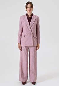 Helles rosa maßgeschneidertes Anzug mit einem doppelt geknöpften Blazer und weitem Hosenbein, das ein dezentes Hundegebissmuster sowie eine kastanienbraune Krawatte aufweist.