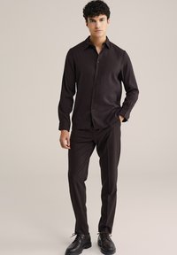 Temno rjava srajca s krokodilskim ovratnikom, slim fit krojem in dolgimi rokavi, v kombinaciji z ujemajočimi se temnimi hlačami in sijočimi črnimi čevlji.