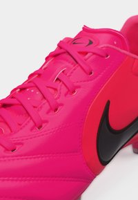 Φωτεινό ροζ ποδοσφαιρικό παπούτσι Nike με μαύρο λογότυπο swoosh και ροζ κορδόνια που ταιριάζουν, εμφανίζεται σε κοντινή, λοξή όψη.