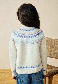 Sweter z wełny dzianinowej w kremowym kolorze z niebieskimi i pomarańczowymi geometrycznymi wzorami wokół dekoltu i dołu. Miękka tekstura, fason z okrągłym dekoltem.