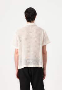 Korte mouwen, opengeweven brei shirt in gebroken wit met een kraag, met een losse pasvorm en kleine, gelijkmatig verdeelde gaatjes in de stof.