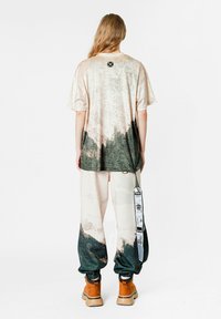 Top de manga corta con un diseño de paisaje degradado en beige y verde oscuro, combinado con pantalones en blanco roto que presentan un patrón similar y puños elásticos.