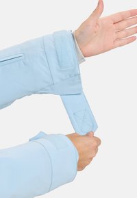 Helle blaue Stoffhülle mit Klettverschlüssen, verstellbarem Riemen und weicher Textur. Verfügt über kontrastierende Nähte und ein funktionales Design.