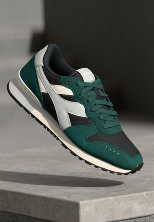 Sneaker sportivo con tomaia in rete nera, dettagli in suede verde e particolari sintetici bianchi. Presenta lacci piatti e una suola in gomma.