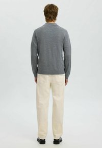 Hall hallide peen, tekstureeritud kudumisega hall sulejope, pikad varrukad ja ümmargune äär, kombineeritud heleda beeži pükste ja mustade kingadega.