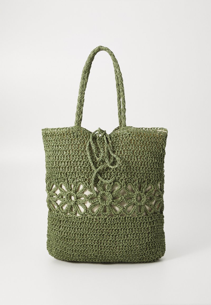 Groene gehaakte tas met geweven handvatten, met een bloemenpatroon in het midden en een trekkoordsluiting aan de bovenkant.