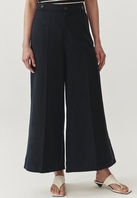 Navy wijde broek gemaakt van zachte stof; heeft twee voorknopen, een hoge taille en een vloeiende silhouet, gecombineerd met lichtgekleurde sandalen.