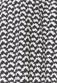 Schwarz-weißer Stoff mit einem Hahnentritt-Muster, einer strukturierten Oberfläche und einem sich wiederholenden Design aus gezackten Formen.
