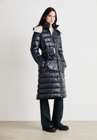 Μαύρο μπουφάν με ελαστική μέση, ψηλό κολάρο και μπεζ λεπτομέρειες στους ώμους. Διαθέτει οριζόντια ραφή και τσέπες στο πλάι.