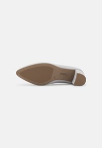 Pompe en cuir gris à bout pointu et à talon bas. La semelle est marron clair avec un grip texturé. Une marque subtile est visible sur la semelle.
