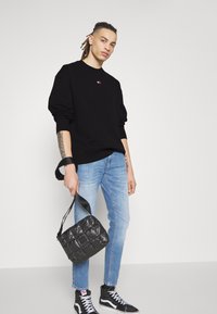 Felpa nera con un piccolo logo, jeans azzurri chiari e borsa a tracolla nera trapuntata. Le scarpe da ginnastica nere alte completano l'outfit.