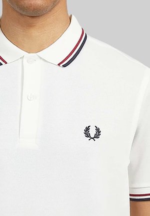 Witte polo met een geribbelde kraag met marineblauwe en rode strepen; geweven stof; geborduurd logo op de linkerborst.
