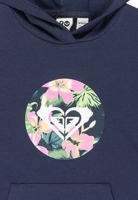 Hoodie bleu marine avec un graphique floral circulaire comprenant des fleurs roses et vertes, et un logo central en forme de cœur blanc. En tissu 100 % coton.