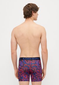 Σλιπ σε μπλε, μωβ και κόκκινο σχέδιο paisley, με ελαστική μέση «BJÖRN BORG» σε μαύρο χρώμα. Το ύφασμα φαίνεται ελαστικό και εφαρμοστό.