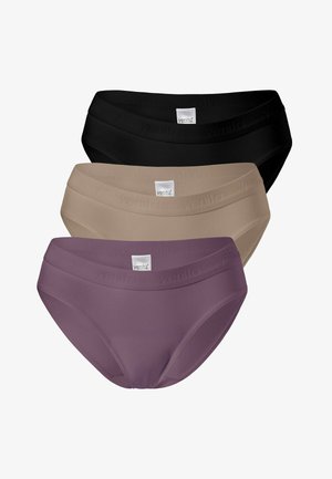 Torso féminin portant des sous-vêtements noirs sans coutures avec une ceinture élastique de marque, les mains reposant sur le haut des cuisses sur un fond uni.