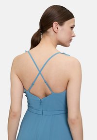 Blaues ärmelloses Kleid mit dünnen, verstellbaren Kreuzträgern und einem Reißverschluss hinten. Glatter Stoff mit schwingendem Textur.