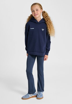 Granatowa bluza z kapturem z logo, w zestawie z dopasowanymi granatowymi legginsami oraz jasnoniebieskimi sneakersami z zygzakowatym wzorem po bokach.