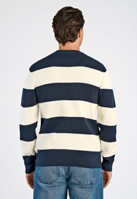 Navy en crèmekleurige gestreepte trui met een ribbelstructuur, ronde halslijn en lange mouwen. Draagt bij lichte blauwe denim jeans.