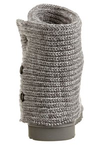 Bota gris de punto con un diseño ligeramente holgado, que presenta tejido texturizado, una parte superior redondeada y dos botones marrones de adorno en el lateral.