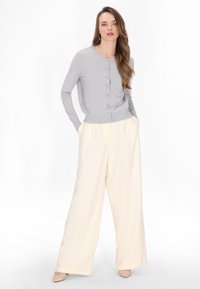 Cardigan grigio a maglia con scollo rotondo e bottoni in perla, abbinato a pantaloni a gamba larga color crema, entrambi con texture morbide.