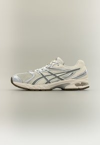 Világosszürke futócipő hálós felsőrésszel, ezüst díszítésekkel, texturált talppal és párnázott középtalppal a tartás és kényelem érdekében.