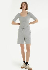 Top grigio aderente a maniche corte con scollo rotondo, abbinato a pantaloni corti grigi con coulisse. Le scarpe sono beige con accenti marroni.