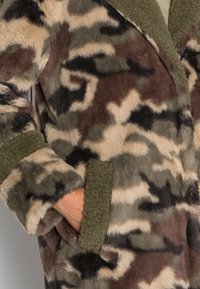 Płaszcz z futerka ekologicznego w kamuflażowy wzór o odcieniach brązu, zieleni i beżu. Charakteryzuje się miękką teksturą, otwartym przodem i naszywanymi kieszeniami.