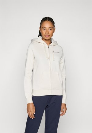Lys kremfarget zip-up hettegenser med snor i hetten, sidelommer og svart logo-broderi på brystet. Mykt stoff og ribbestrikkede mansjetter.