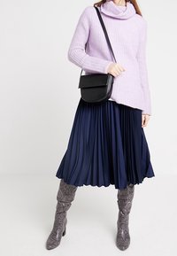 Maglione a maglia viola chiaro con scollo a barchetta, abbinato a una gonna plissettata blu navy e stivali al ginocchio in python grigio. Inclusa una borsa a tracolla nera.
