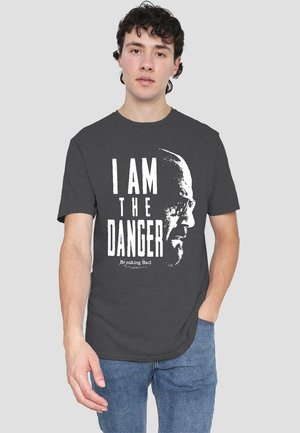 Dunkelgraues Baumwoll-T-Shirt mit einem weißen Grafikdruck, der den Text "ICH BIN DIE GEFAHR" und eine Profil-Illustration zeigt. Kurze Ärmel, runder Halsausschnitt.