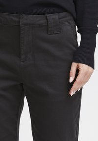 Črne hlače iz bombažne mešanice z ravnim sprednjim delom, stranskimi žepi in gladko teksturo. Pas vsebuje zanke za pas, kar omogoča prilagodljivo prilegajočost.