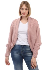 Cárdigan rosa de punto con un diseño texturizado y mangas acanaladas, usado sobre una camisa blanca, combinado con jeans azules.