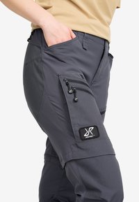 Grå cargobyxor tillverkade av hållbar tyg med sidfickor, dragkedjor och en logopatch. Har en figurnära design med elastiska detaljer.