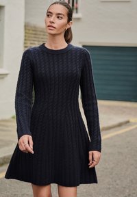 Marineblå strikket kjole med ribbet tekstur, lange ærmer, rund halsudskæring og udvidet nederdel. Enkel design uden markante pynt.